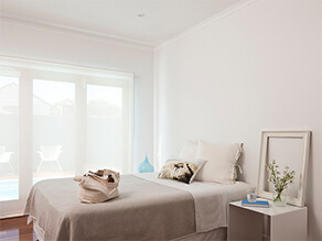 Neutral modern simplistic bedroom with beige bed covers white pillows with plant on bedside table